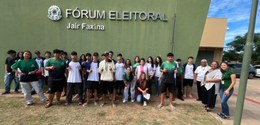 Fotografia que retrata um grupo de jovens e adultos posando em frente à fachada do fórum eleitor...
