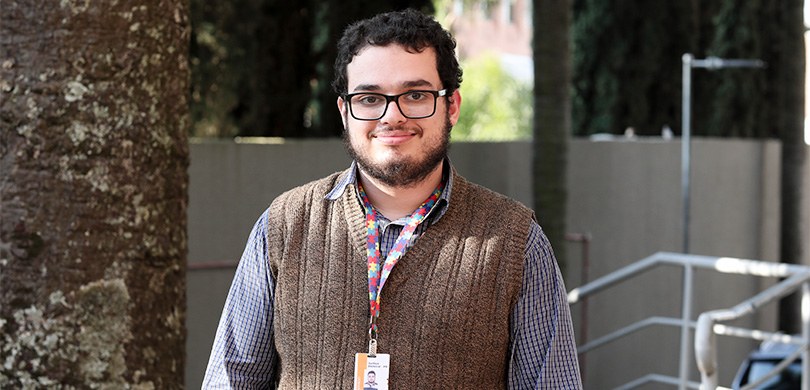 13 de julho, Dia Mundial do TDAH Fotografia de Rafael, um jovem com olhos castanhos, cabelos castanhos curtos e barba. Ele usa óc...