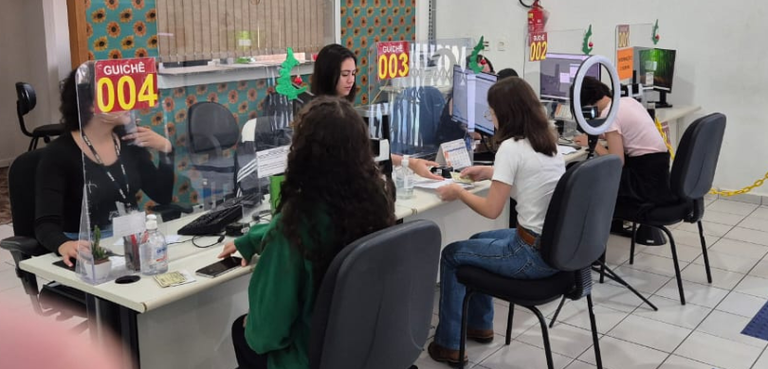14ª Zona Eleitoral de Ponta Grossa realiza projeto para conscientizar o voto jovem nas eleições 3 Fotografia de três estudantes sentadas em cadeiras pretas diante de guichês, recebendo atendimen...