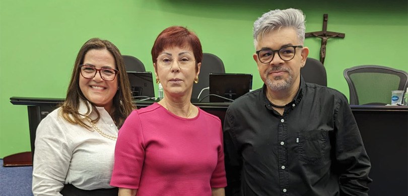 Fotografia de duas mulheres e um homem posando para foto. Uma das mulheres tem cabelo loiro e us...