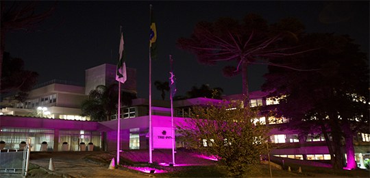 Na imagem a fachada de um prédio durante o período noturno com a iluminação da cor rosa.