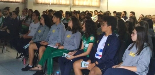 Na imagem alunos sentados acompanhando uma palestra.