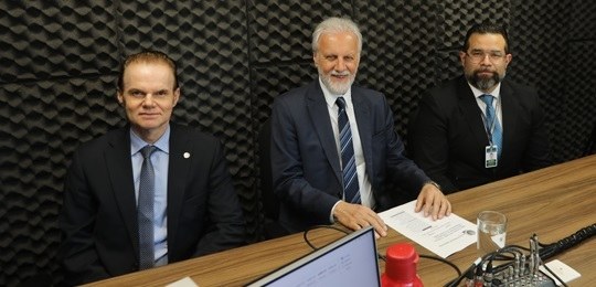 Três homens em um estúdio de rádio posam para foto. 