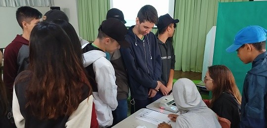 Várias crianças ao redor de uma urna eletrônica realizando uma simulação de votação.