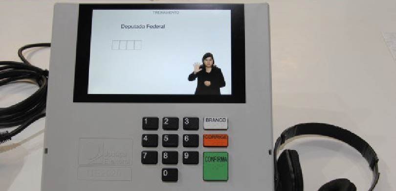 Uma urna eletrônica mostrando na tela uma intérprete de libras no canto inferior direito da tela.