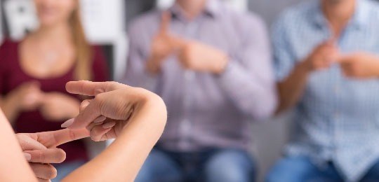 Imagem de uma pessoa ensinando um sinal em Libras para outras três pessoas