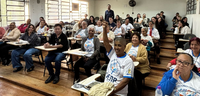 Fotografia em ambiente interno que retrata uma sala de aula de formato anfiteatro repleta de pes...