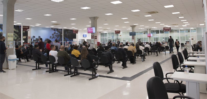 Foto de um grande salão em que se observam, ao centro, várias pessoas sentadas de costas em cade...