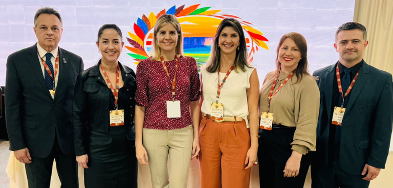 Fotografia de quatro mulheres, que vestem roupas formais nas cores verde, bege, vermelho, laranj...
