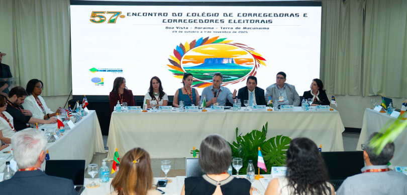Na imagem veem-se homens e mulheres sentados em uma mesa com toalhas brancas. No fundo, lê-se “5...