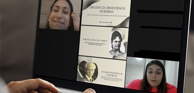 Fotografia da tela de um notebook durante uma videoconferência. É possível ver duas mulheres com...