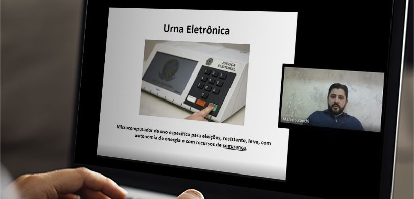  Fotografia da tela de um notebook durante uma videoconferência. É possível ver uma apresentação...