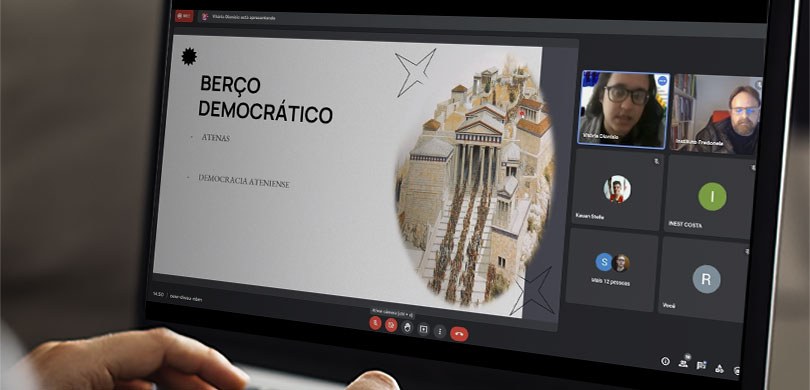 Fotografia da tela de um notebook durante uma videoconferência. É possível ver duas pessoas com ...
