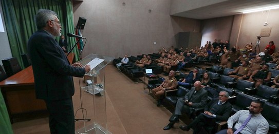 Um homem, que veste terno, está falando em um púlpito enquanto uma plateia o assiste.