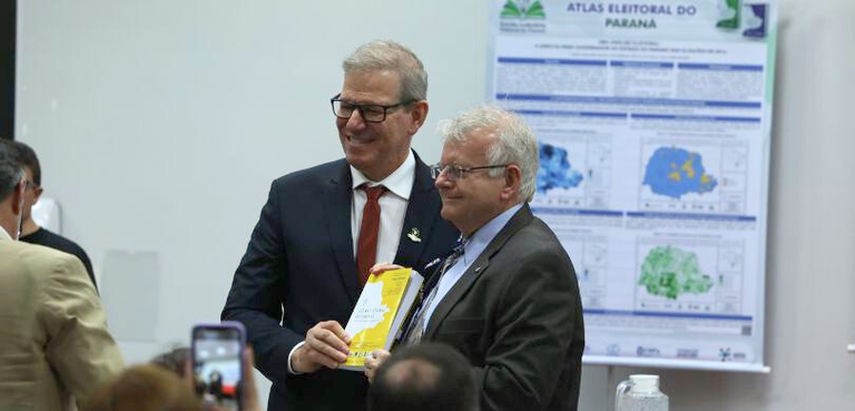 Fotografia em que se vê o presidente Sigurd recebendo das mãos do reitor da Unicentro um exempla...