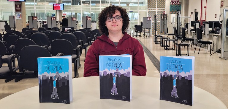 Fotografia de um jovem de pele clara e cabelos cacheados, que usa óculos e veste uma jaqueta de ...