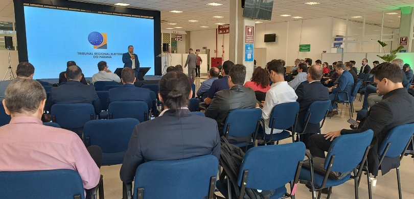 Abertura de congresso sobre IA no Judiciário reúne especialistas de todo o país na CAE de Curitiba Fotografia de um homem de terno azul e camisa branca falando em um palco diante de uma plateia, ...