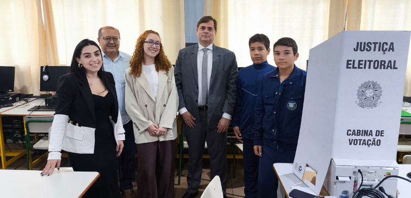Fotografia de duas moças, dois homens e dois adolescentes posando sorrindo em uma sala de aula, ...