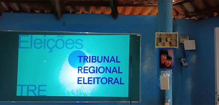 Fotografia de dentro da oca, com um telão com slides azul, escrito: Eleições - Tribunal Regional...