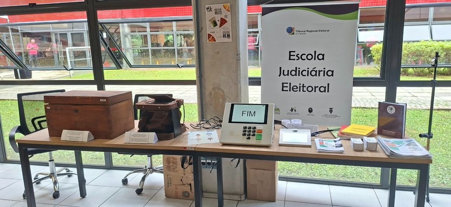 Fotografia em que se observa uma mesa retangular de madeira com diversos itens organizados sobre...