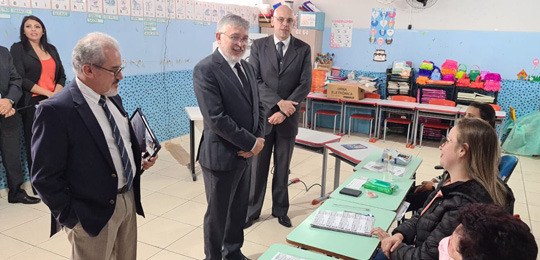 foto de três homens de terno e gravata em frente a uma mesa de recepção de votos, em uma seção e...