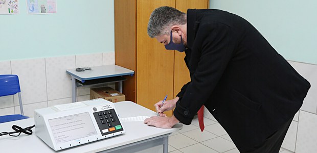 Foto de um homem conferindo a zerésima ao lado de uma urna eletrônica