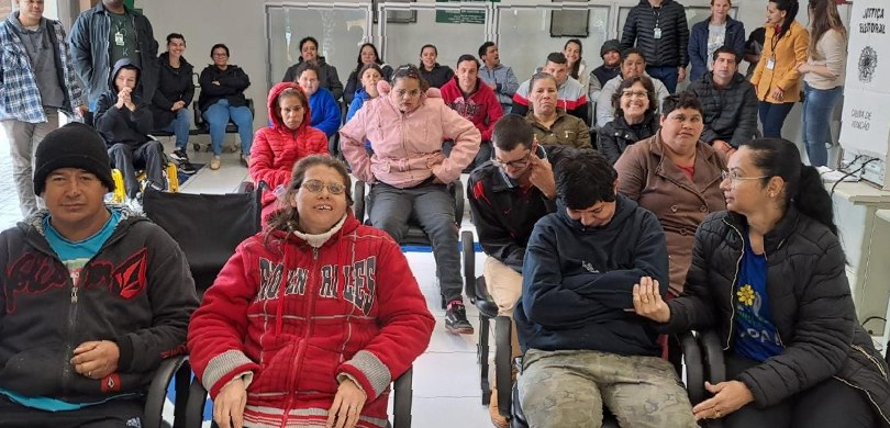 Fotografia de uma sala com diversas pessoas, entre homens e mulheres. Algumas delas aparecem sen...