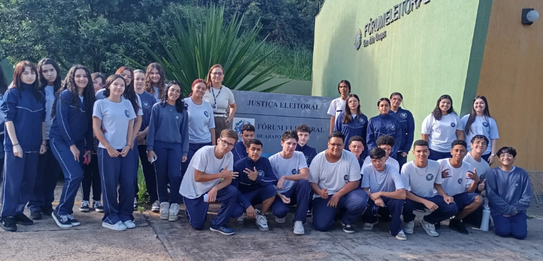 Fotografia que retrata um grupo de jovens posando para uma foto em frente à fachada do Fórum Ele...