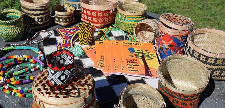 Fotografia das cartilhas do TRE-PR empilhadas sobre uma toalha cinza, com detalhes em branco e p...