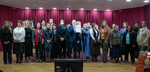 Fotografia de um grupo de pessoas posando para foto no palco de um auditório. Um homem e uma mul...