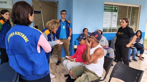 Fotografia de um grupo de indígenas sentados em uma central de atendimento ao eleitor.