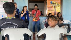 Em uma sala, um grupo de pessoas está reunido para uma apresentação ou discussão. Uma mulher de ...