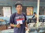 Um homem com uma camiseta escura, pulseiras indígenas e cabelo bagunçado está no centro, olhando...