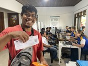 Um homem sorridente de camisa vermelha, segurando um documento de eleitor que exibe diretamente ...