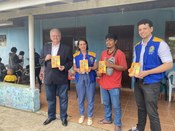 Quatro pessoas estão lado a lado em frente a uma casa de cor azul, olhando para a câmera e segur...