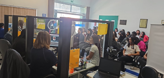 Fotografia de um homem e duas mulheres sentados em cadeiras azuis diante de mesas brancas sobre ...