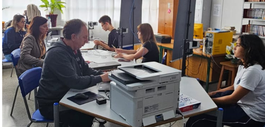 Fotografia de um homem e duas mulheres sentados em cadeiras azuis diante de mesas brancas sobre ...