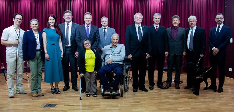 Foto em que aparecem várias pessoas, com e sem deficiência, entre homens e mulheres, posando sob...