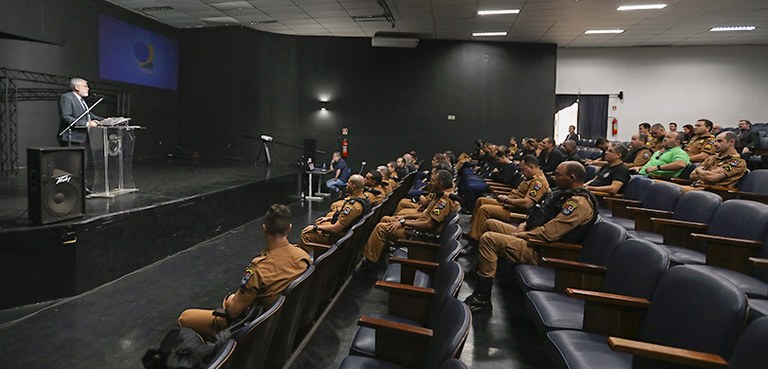 Fotografia de um auditório, com um homem falando em um púlpito. Na plateia, a maioria das pessoa...
