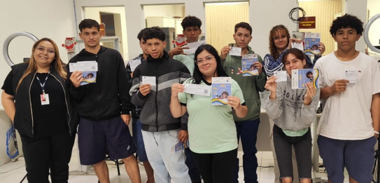 Fotografia de uma mulher em pé palestrando para jovens uniformizados em uma sala de aula com par...