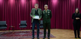 Fotografia em que aparecem dois homens posando no palco do auditório do TRE-PR. Um deles mostra ...