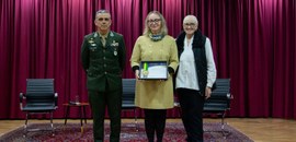 Fotografia em que aparecem duas mulheres e um homem posando no palco do auditório do TRE-PR. Uma...