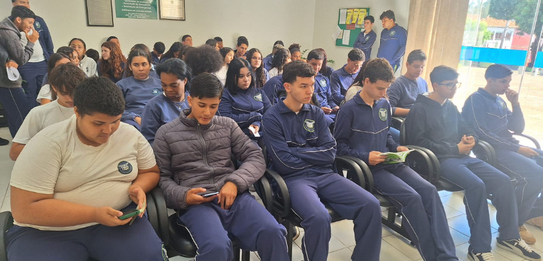 Fotografia de uma mulher em pé palestrando para jovens uniformizados em uma sala de aula com par...
