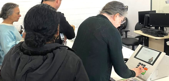 Fotografia na qual se vê uma pessoa pressionando a tecla verde de uma urna eletrônica de cor cla...