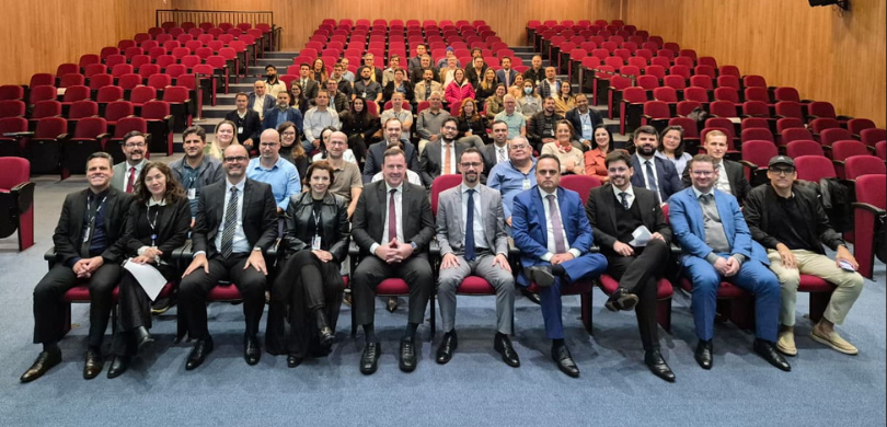 Fotografia em ambiente interno na qual se observa um grande grupo, composto por homens e mulhere...