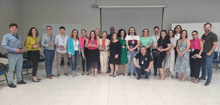 Capacitação sobre prevenção e enfrentamento do assédio é realizada no Fórum Eleitoral de Curitiba Vários homens e mulheres estão perfilados. Alguns deles seguram um livro de capa azul. Atrás del...