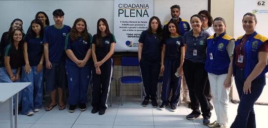 Fotografia de uma mulher em pé palestrando para jovens uniformizados em uma sala de aula com par...