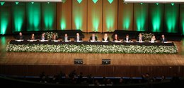 Fotografia da mesa de autoridades em um auditório. Na mesa, estão 13 pessoas, entre homens e mul...