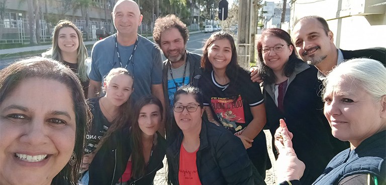 Fotografia, em estilo selfie, de oito mulheres e três homens posando sorrindo. Algumas pessoas u...