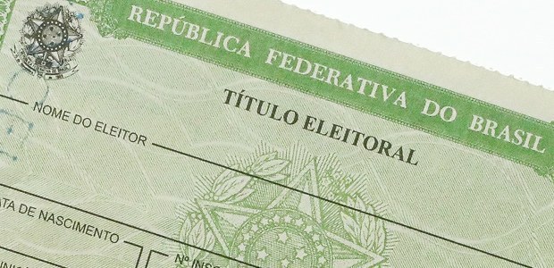 Fotografia de parte de um Título Eleitoral. O documento é verde, com ilustrações do Brasão da Re...